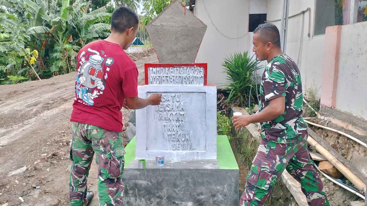 Babinsa Kopda Jefri Samana dan Pratu Muhyidin tampak fokus mengecat tugu TMMD, bagian dari program pembangunan di Desa Ombulodata
